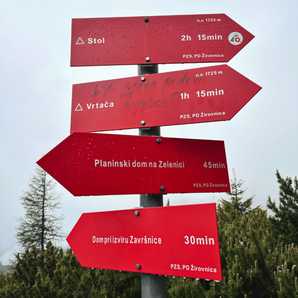 Red hiking trail signs in the Karawanks mountains showing directions to Stol, Vrtača and mountain huts.